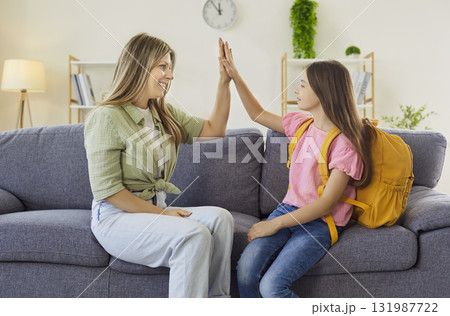 Happy mom and schoolgirl give a high five on sofa before classes, cheerful mood 131987722