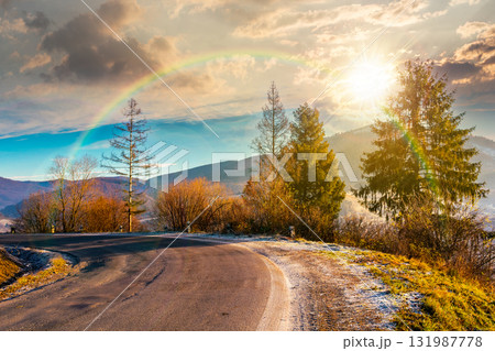 country road in mountains at sunset. beautiful countryside landscape in late autumn. fir trees on the roadside in evening light. scenic view of blue sky with clouds above the distant ridge in snow 131987778