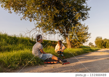 Children spend their free time inline skating on a path surrounded by greenery, sharing laughter and friendship under the warm sunlight 131988489