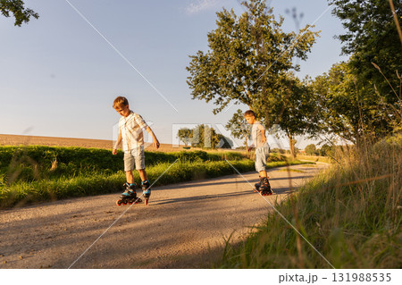 Two children laugh and skate on inline skates along a quiet country path. Bright sunlight illuminates the green landscape, creating a cheerful outdoor scene Two children laugh and skate on inline skates along a quiet country path. Bright sunlight illuminates the green landscape, creating a cheerful outdoor scene 131988535