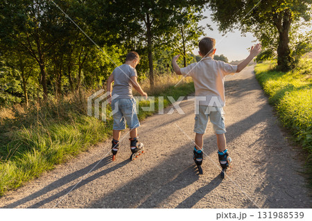 Two friends are happily inline skating along a sunlit path surrounded by trees. They are enjoying their time outdoors on a warm day, filled with laughter and friendship 131988539