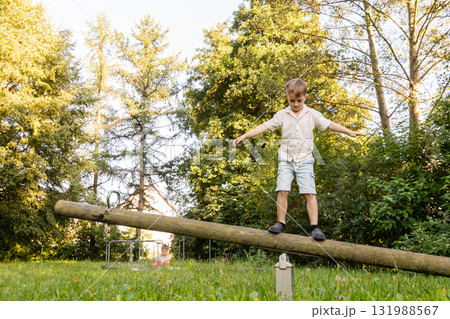 Two children are playing outside in a lush park. One child balances on a log while the other plays nearby, enjoying the sunny weather and the beauty of nature Two children are playing outside in a lush park. One child balances on a log while the other plays nearby, enjoying the sunny weather and the beauty of nature 131988567