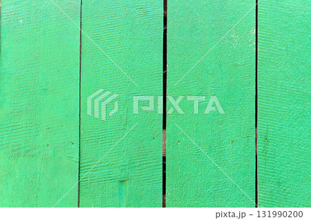 Green painted wooden fence with visible vertical planks and natural wood texture. Surface shows rough grain patterns, small cracks, and gaps between boards, creating rustic outdoor background 131990200