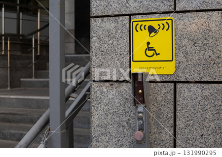 Yellow accessibility sign. Indicates call system with bell and is positioned on wall near stairs, with visible button to activate system. Offering assistance in public spaces Yellow accessibility sign. Indicates call system with bell and is positioned on wall near stairs, with visible button to activate system. Offering assistance in public spaces 131990295
