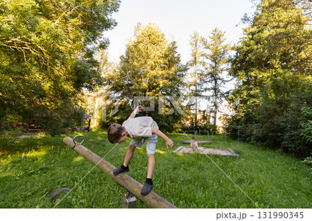 Two children play happily in a park surrounded by trees. One child balances on a log while the other plays nearby, enjoying a sunny afternoon in nature Two children play happily in a park surrounded by trees. One child balances on a log while the other plays nearby, enjoying a sunny afternoon in nature 131990345