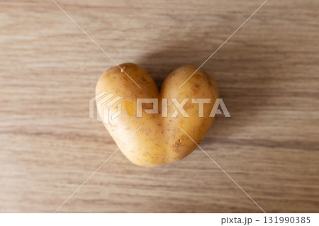 A heart-shaped potato sits on a wooden surface, displaying its unusual shape. This interesting vegetable can spark creativity in cooking or simply serves as a quirky decoration 131990385