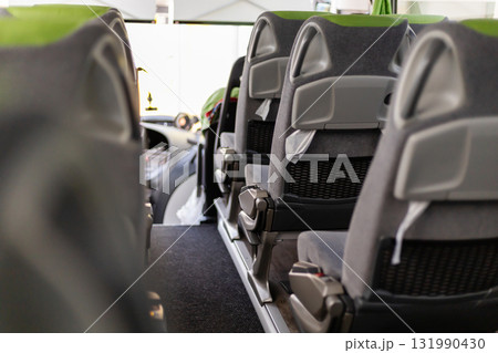 Inside a bus, the scene captures empty, modern seats arranged tidily along the aisle. Bright daylight streams through the large windows, creating an inviting atmosphere 131990430