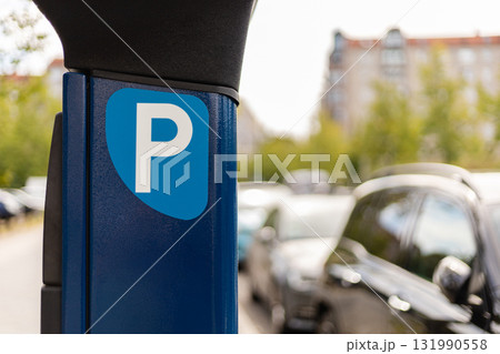 A parking meter is prominently displayed next to several parked cars in a bustling urban environment on a bright, sunny day. Trees and buildings are visible in the background A parking meter is prominently displayed next to several parked cars in a bustling urban environment on a bright, sunny day. Trees and buildings are visible in the background 131990558