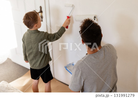 A man and his young son are painting the walls of their bedroom. They are whitewashing the walls as part of a home improvement project. The boy actively helps his father A man and his young son are painting the walls of their bedroom. They are whitewashing the walls as part of a home improvement project. The boy actively helps his father 131991279