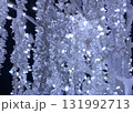 A mesmerizing, close-up vertical shot of crystal-like LED Christmas lights illuminated in a bright, cool white and icy blue glow against a deep black night sky. 131992713