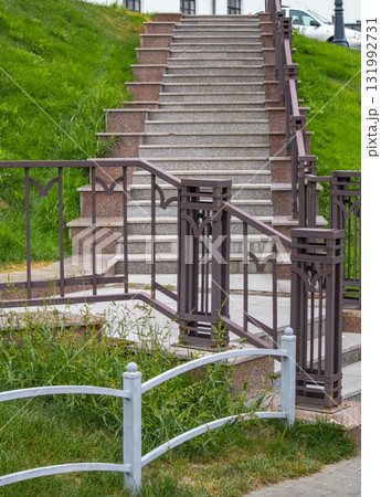 Granite staircase with wrought iron railings on green slope 131992731