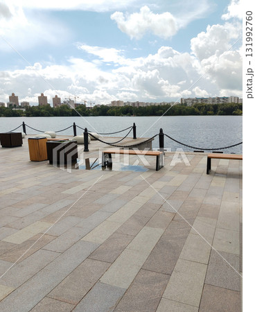 Urban waterfront with benches and river view under a cloudy sky Urban waterfront with benches and river view under a cloudy sky 131992760
