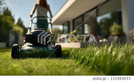 A dedicated woman actively mows the lush green lawn with a powerful gasoline lawnmower on a sunny day, emphasizing yard work and home maintenance. AI Generated 131993633