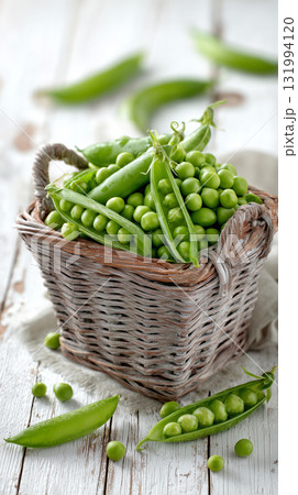 Fresh green peas in a wicker basket with scattered pods around 131994120