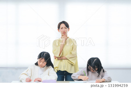 勉強する二人の女の子の後ろで悩む女性 勉強する二人の女の子の後ろで悩む女性 131994259