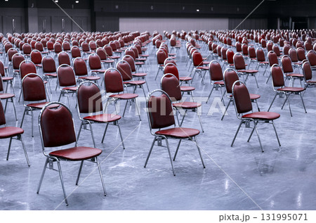 Rows of empty red chairs in a vast conference hall, neatly arranged and waiting for a large business meeting or corporate event setup 131995071