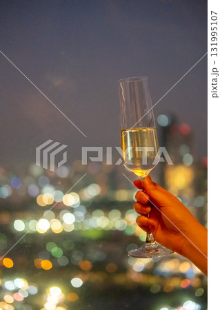 A hand holding a glass of Prosecco or sparkling wine with colorful sunset sky and city view on the background A hand holding a glass of Prosecco or sparkling wine with colorful sunset sky and city view on the background 131995107