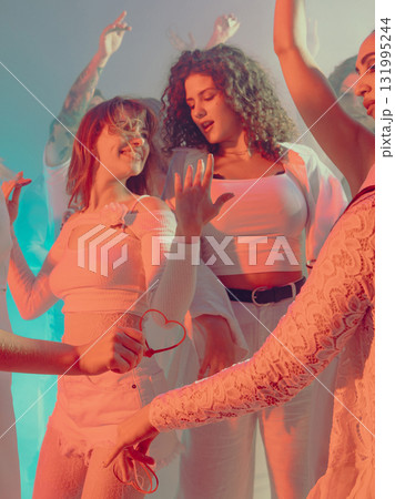Women dancing joyfully at white party in warm romantic light. 131995244
