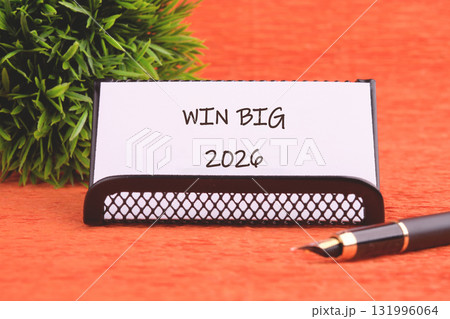 A message on a desk states WIN BIG 2026, next to a decorative plant and pen on a textured orange surface suggesting planning and a promising future 131996064