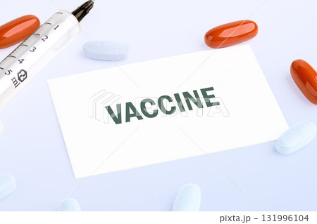 Close-up shows a card with Vaccine on it, surrounded by pills and a syringe. Medicines give hope for improved health and well-being on a white surface 131996104