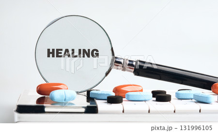 A magnifying glass focuses on the word HEALING as pills rest on a white surface. This suggests exploring medical solutions for wellness and recovery 131996105