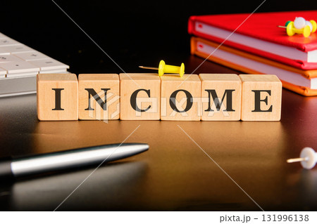 Wooden blocks spelling INCOME sit on a desk, with a pen, push pins, keyboard and financial books nearby, suggesting financial strategy and office planning Wooden blocks spelling INCOME sit on a desk, with a pen, push pins, keyboard and financial books nearby, suggesting financial strategy and office planning 131996138