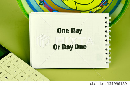 A notepad displaying One Day Or Day One sits near a calculator and a colorful clock, all against a green background, suggesting thoughts about starting goals now A notepad displaying One Day Or Day One sits near a calculator and a colorful clock, all against a green background, suggesting thoughts about starting goals now 131996189