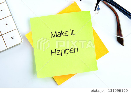 Lime and yellow notes stacked show Make It Happen in black text. Glasses and a calculator rest nearby on a white surface. A motivational reminder on your desk 131996190