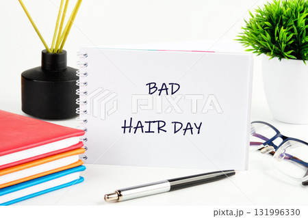 A notepad on a bright desk reads bad hair day. Near it are books, a pen, glasses, a plant, and a reed diffuser in a black vase, suggesting morning routines or study 131996330