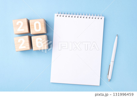 Wooden cubes with numbers for the New Year 2026 with a notebook and pen on a blue background 131996459