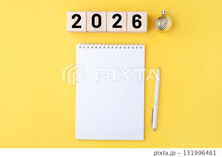 Wooden cubes with numbers for the New Year 2026 with a notebook and pen on a yellow background 131996461