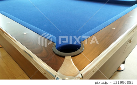 A hole in the corner of a pool table with a wooden border. and covered with a blue flannel cloth. 131996883