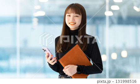 スマートフォンとバインダーを持つ笑顔の女性・ビジネスウーマン スマートフォンとバインダーを持つ笑顔の女性・ビジネスウーマン 131998516