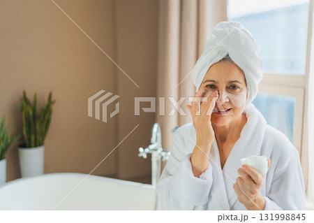 Mature adult old woman applying nourishing anti age face cream doing daily beauty routine. Senior woman with white mask or creme on skin gets facial treatment Skin care aging beauty skincare cosmetics 131998845