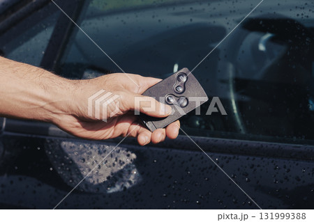 Hand using keyless remote to unlock wet car door 131999388