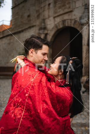 Interracial couple embracing in traditional Chinese wedding attire Interracial couple embracing in traditional Chinese wedding attire 131999632