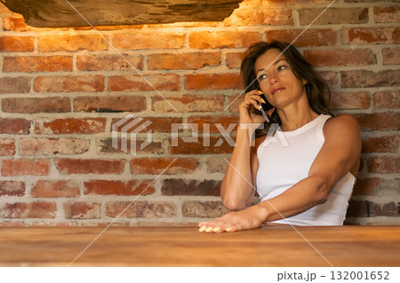 A woman engages in a thoughtful conversation over the phone, framed by an inviting and charming brick backdrop 132001652