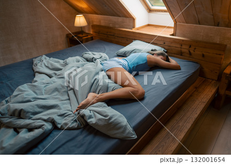 In a serene attic bedroom, a person is peacefully resting among soft and cozy bedding, surrounded by tranquility 132001654