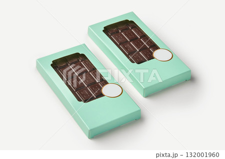 Two dark chocolate bars resting in light green boxes on white background 132001960