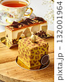 Delicious modern cakes with gold decorations resting on wooden table near teacup 132001964
