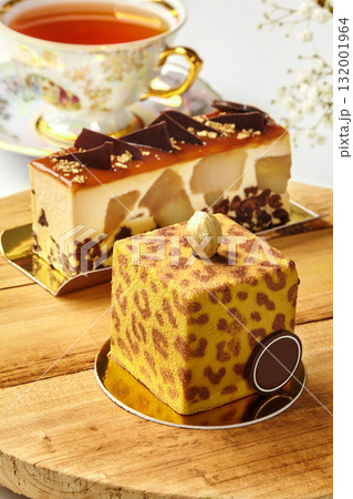 Delicious modern cakes with gold decorations resting on wooden table near teacup Delicious modern cakes with gold decorations resting on wooden table near teacup 132001964