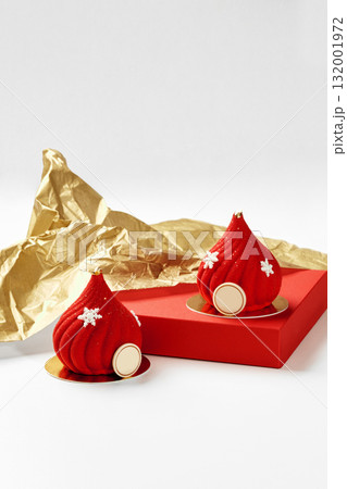 Two red christmas mousse cakes decorated with snowflakes and gold details resting on red surface with gold wrapping paper 132001972
