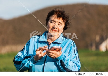 International Day of Older Persons. Portrait of an elderly happy woman typing at smartphone in her hand. The concept of studying modern technologies by pensioners 132002079