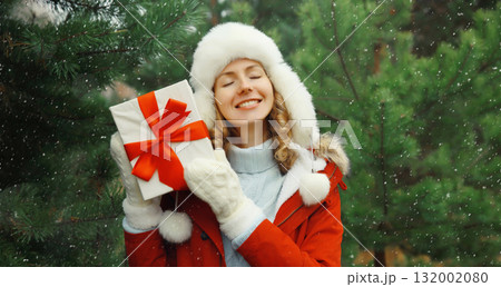 Happy smiling young woman holding red gift box on Christmas tree background in winter forest Happy smiling young woman holding red gift box on Christmas tree background in winter forest 132002080