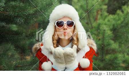 Happy young woman in winter park against Christmas tree, girl in white hat, glasses in snowy forest 132002081