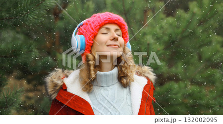Happy young woman enjoy listening to music with headphones in winter forest against Christmas tree Happy young woman enjoy listening to music with headphones in winter forest against Christmas tree 132002095