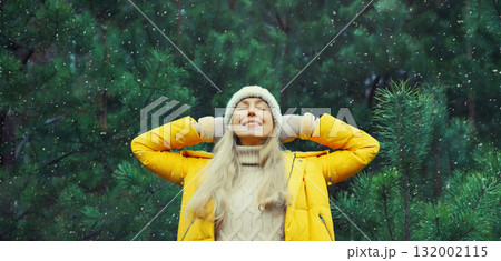 Winter day, happy smiling woman enjoys snow, warm weather against Christmas tree in snowy forest 132002115