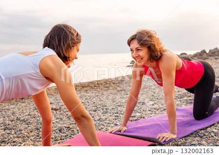 Fitness and wellness. Two Caucasian Happy women training on mat at beach 132002163