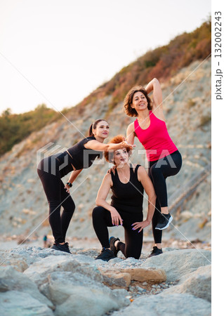 Three adult athletic Caucasian happy women in sportswear posing standing on rock. Vertical. Wellness and sport lifestyle 132002243