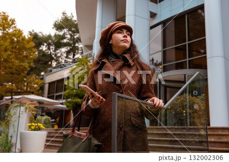 Elegant motion through the city as a young woman walks alone, holding her smartphone and embracing autumn. Bottom view 132002306